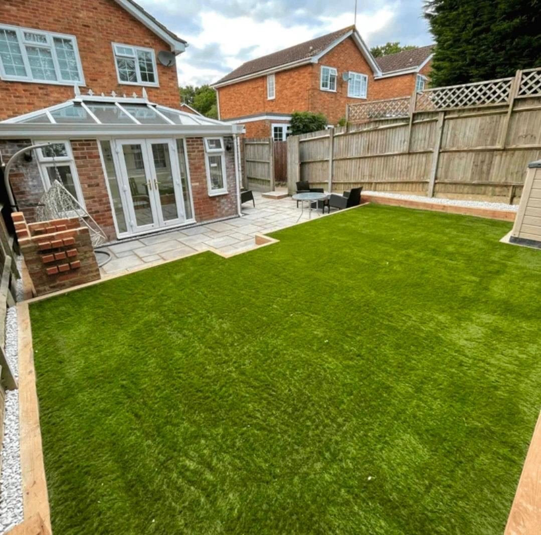 Garden landscaping with patio and artificial lawn beside conservatory